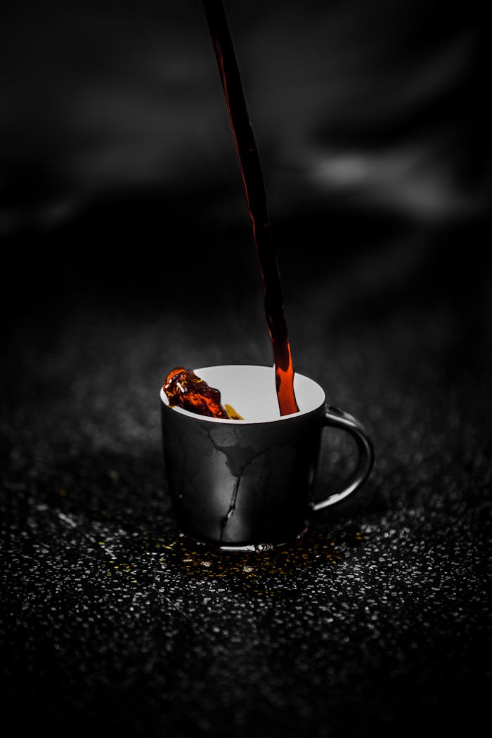 digital Close-up of steaming dark coffee being poured into a black cup on a dark textured surface. Rich aroma.