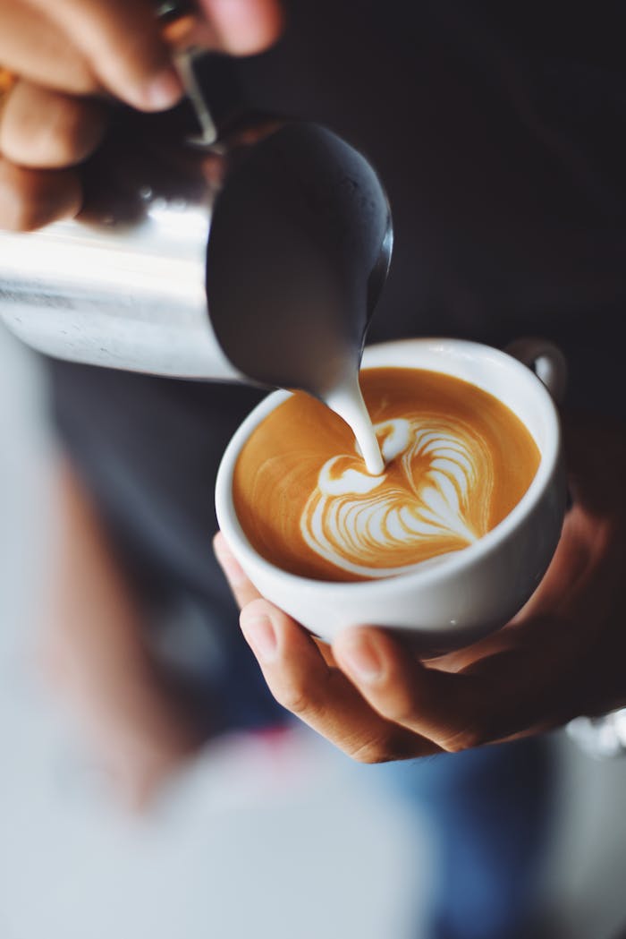 Services-03 Close-up of barista pouring milk to create stunning latte art in a coffee shop setting.