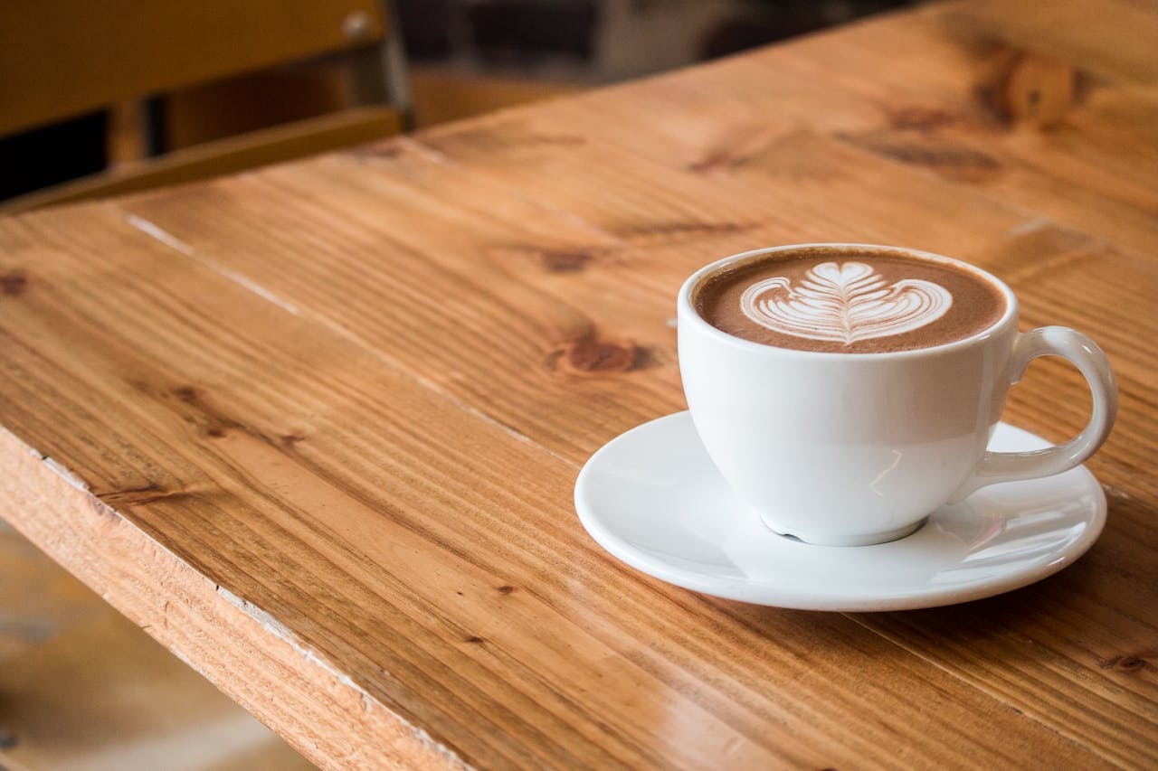 creative-02 Close-up of a white cup of latte with artistic foam on a rustic wooden table.